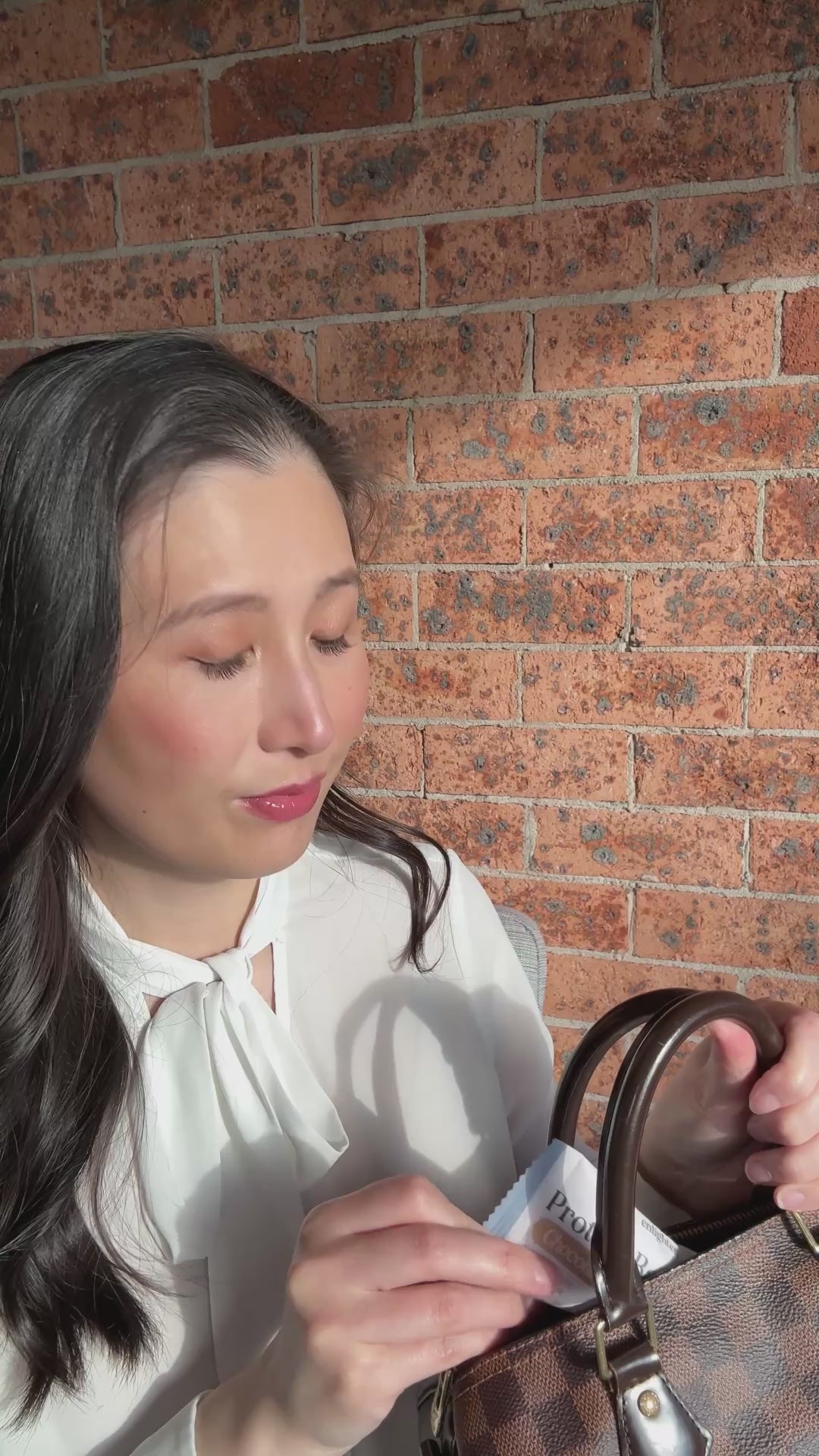 Video of Dr Angela Kwong taking an Enlighten Me Protein Ball from her handbag, unwrapping it and enjoying it as a quick, convenient, handbag-sized snack on the go.